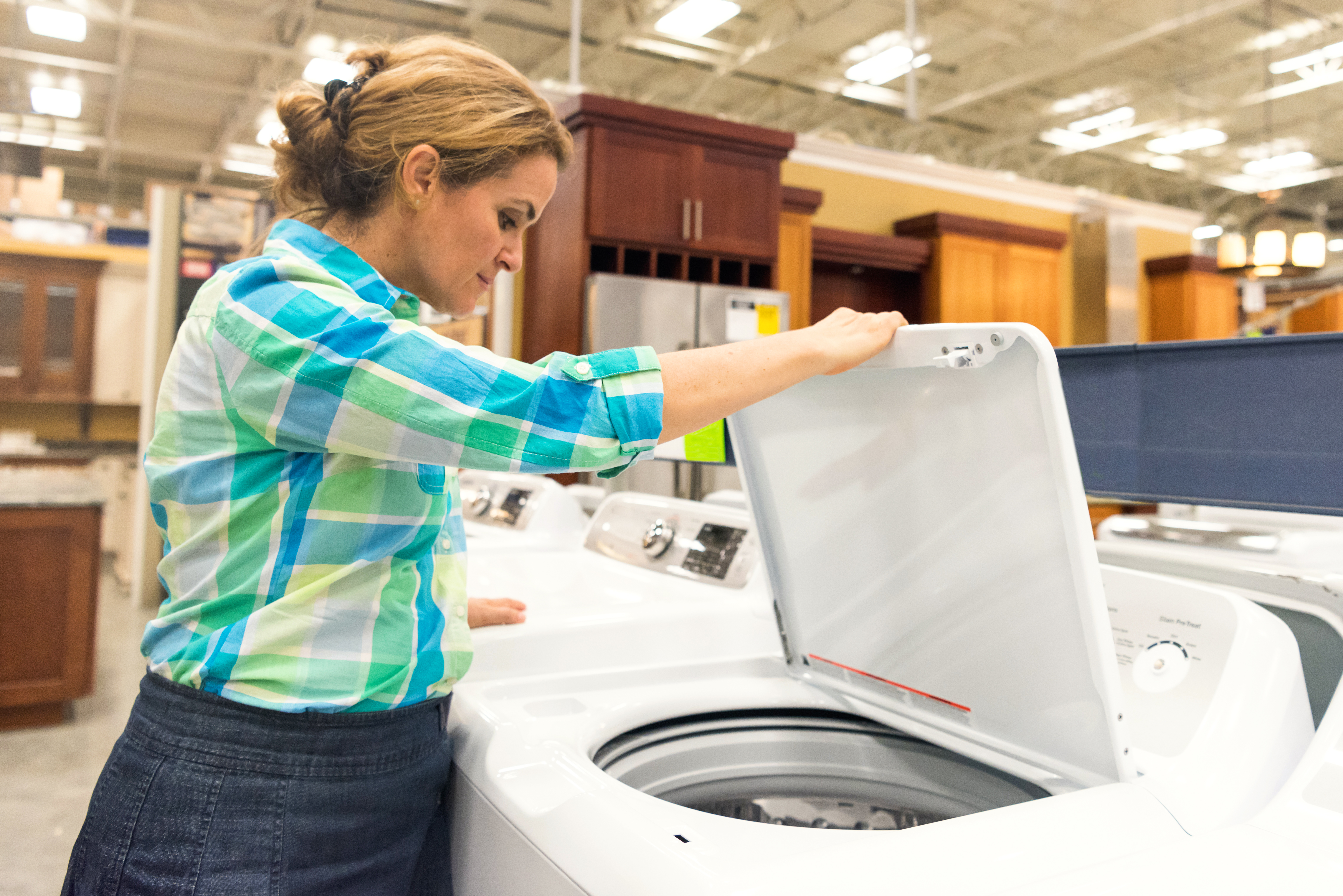 Woman in a plaid shirt looking into a top load washer in an appliance store 